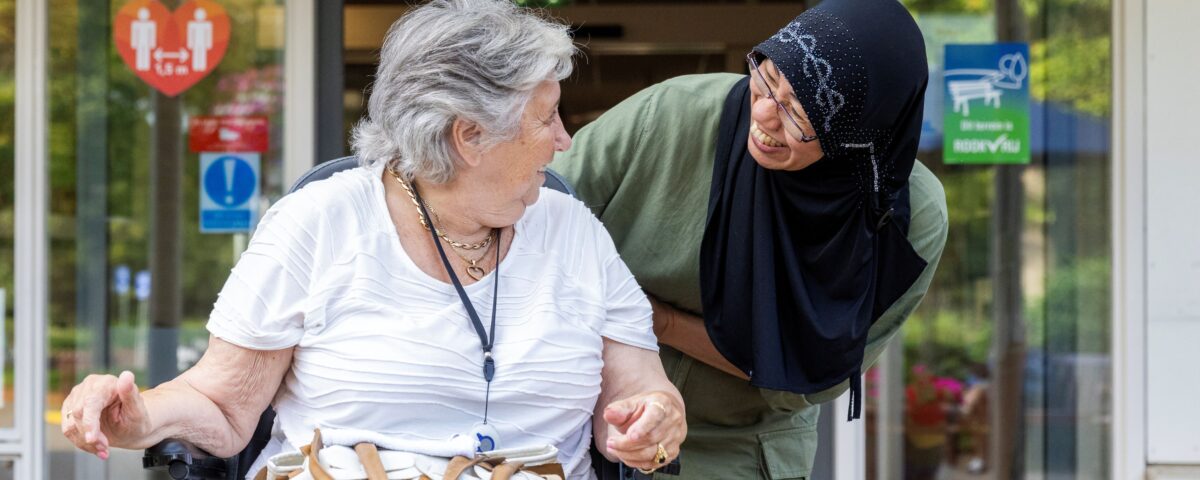Vrouw met oudere vrouw in rolstoel buiten voor verpleeghuis Kennemerhart