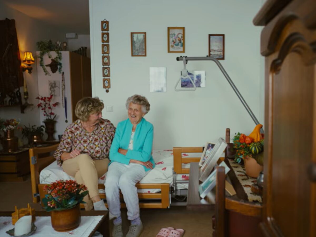 Persoon en oudere persoon zitten naast elkaar op een bed.