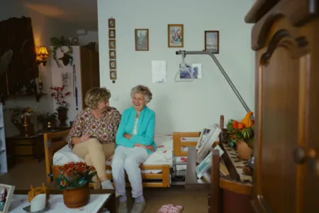 Persoon en oudere persoon zitten naast elkaar op een bed.