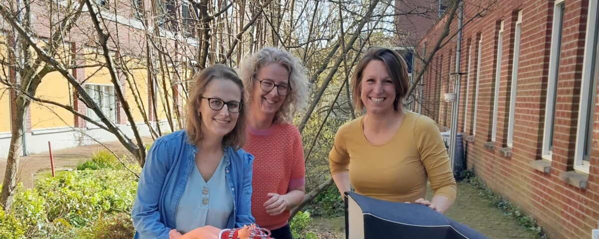 3 collega's staan buiten voor een kinderwagen met een pop