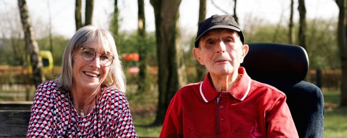 Vrouw zit naast man in rolstoel buiten
