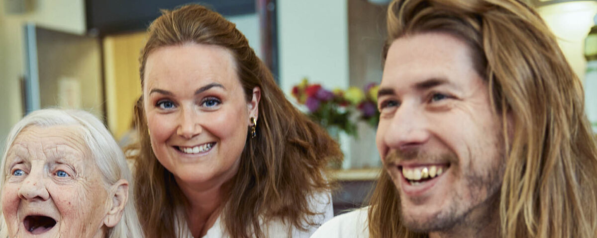 Oudere vrouw zit lachend met twee jonge mensen