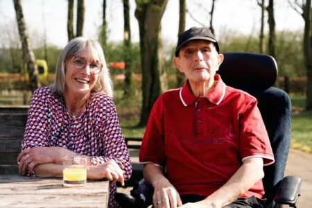 Vrouw zit naast man in rolstoel buiten