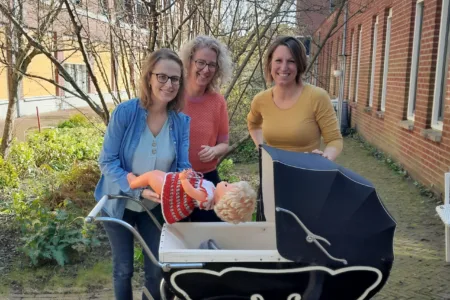 3 collega's staan buiten voor een kinderwagen met een pop